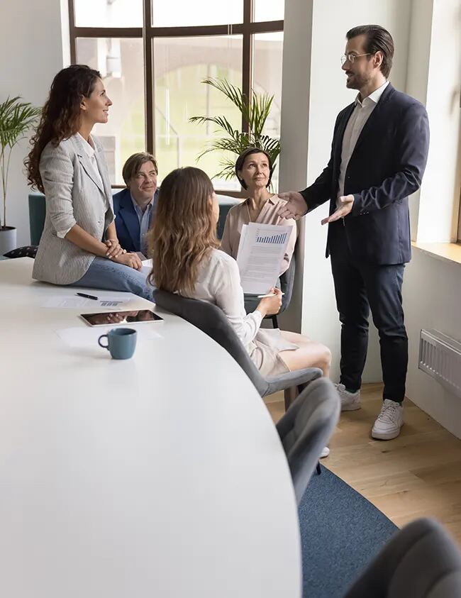 A presenter speaking with colleagues around a meeting table