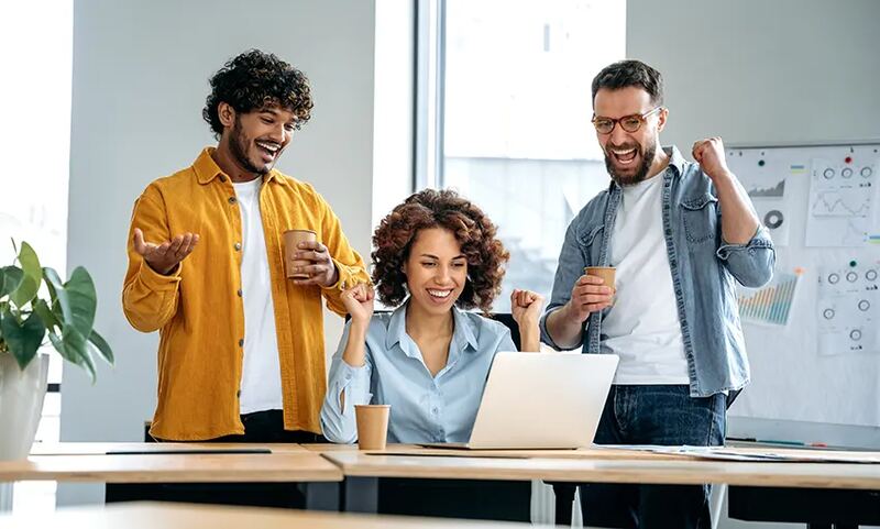 A team celebrating a success around a laptop