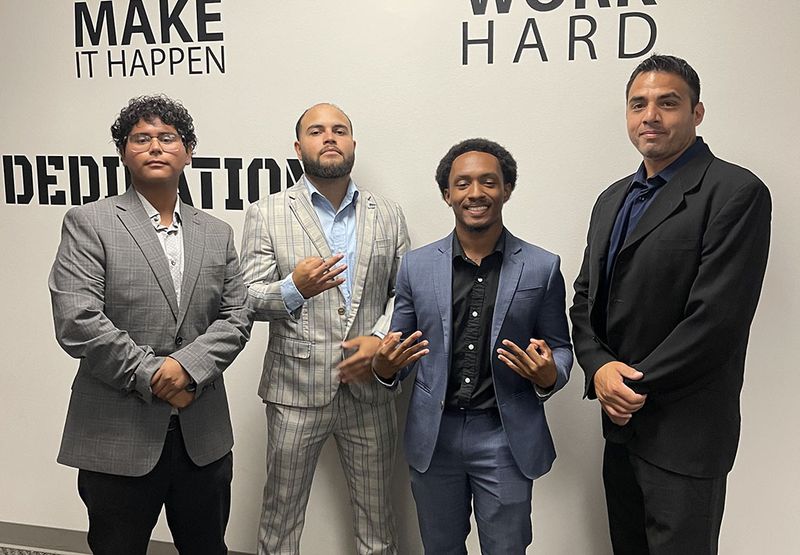 Mission III Management team members in front of a “Make It Happen — Work Hard” wall