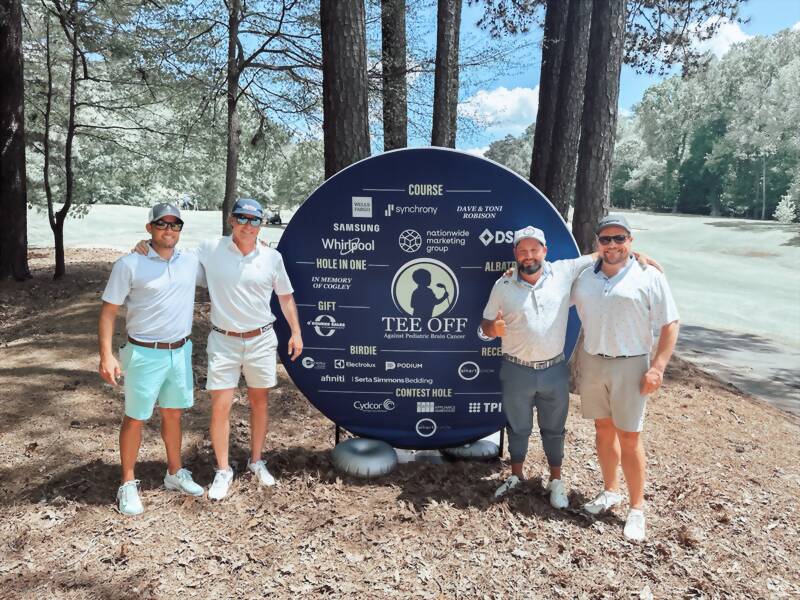 New Acquisitions team members at the Tee Off Against Pediatric Brain Cancer sign during the J. Paul Austin Invitational golf tournament in Atlanta