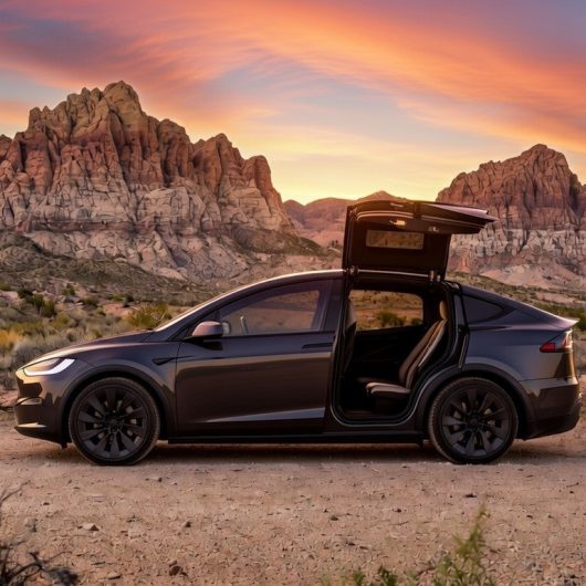 Tesla Model X with its falcon-wing doors open on a desert road at Red Rock Canyon at sunset
