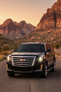 Black Cadillac Escalade ESV parked on a desert road below the Red Rock Canyon cliffs