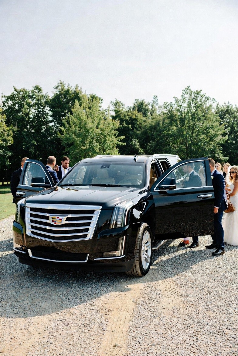Black Cadillac Escalade with its doors open at an outdoor wedding as the party boards