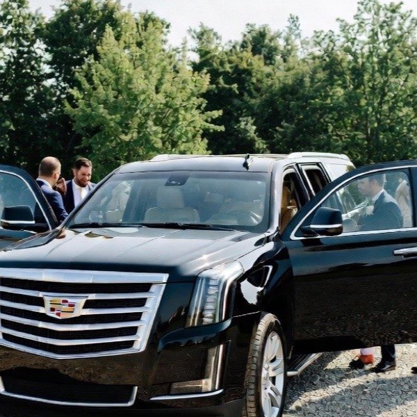 Black Cadillac Escalade with its doors open at an outdoor wedding as the party boards