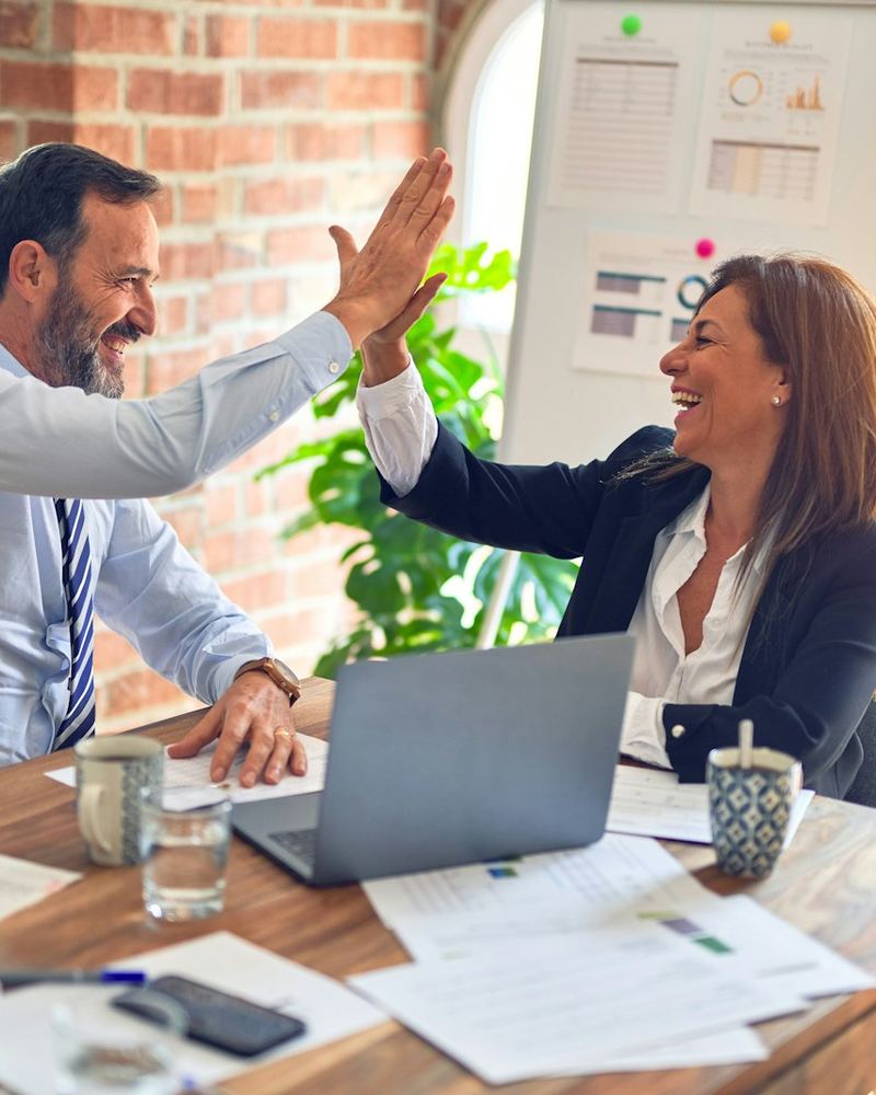 Two colleagues celebrating a new hire with a high five at their desk