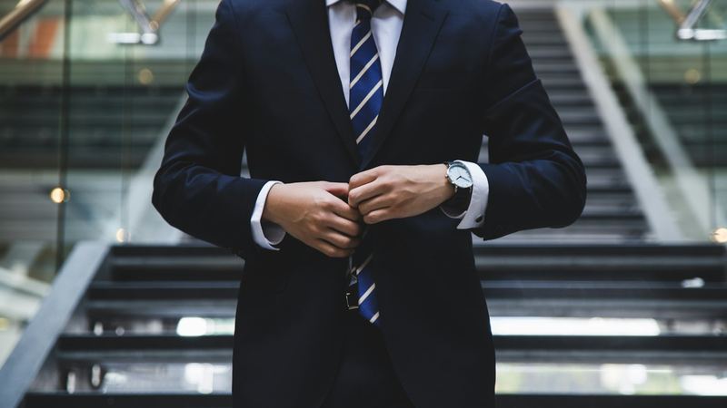 Sales leader in a navy suit buttoning his jacket on an office staircase