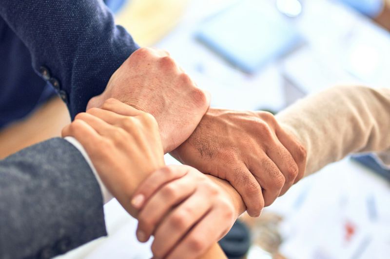 Client success team joining hands over a project table
